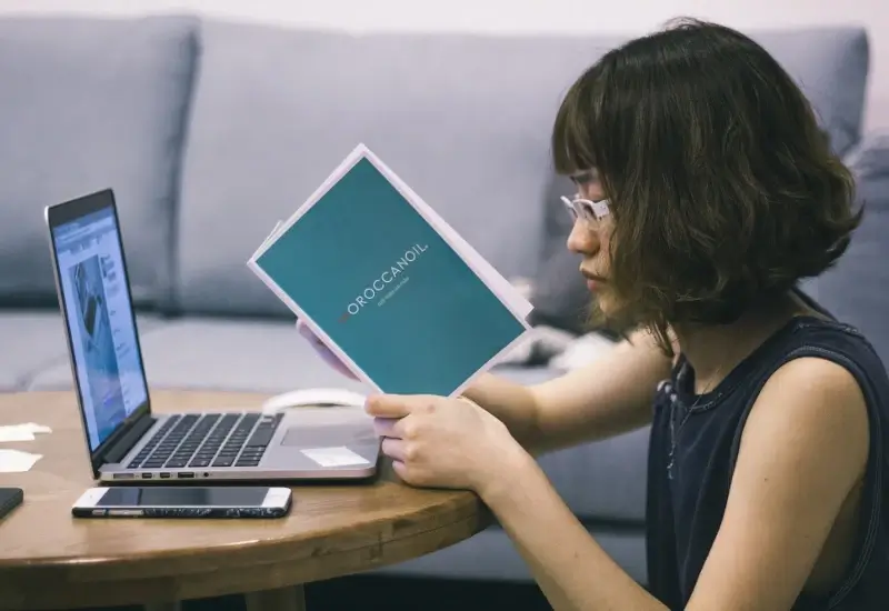 A person sitting on the floor in front of a small table with a laptop while reading