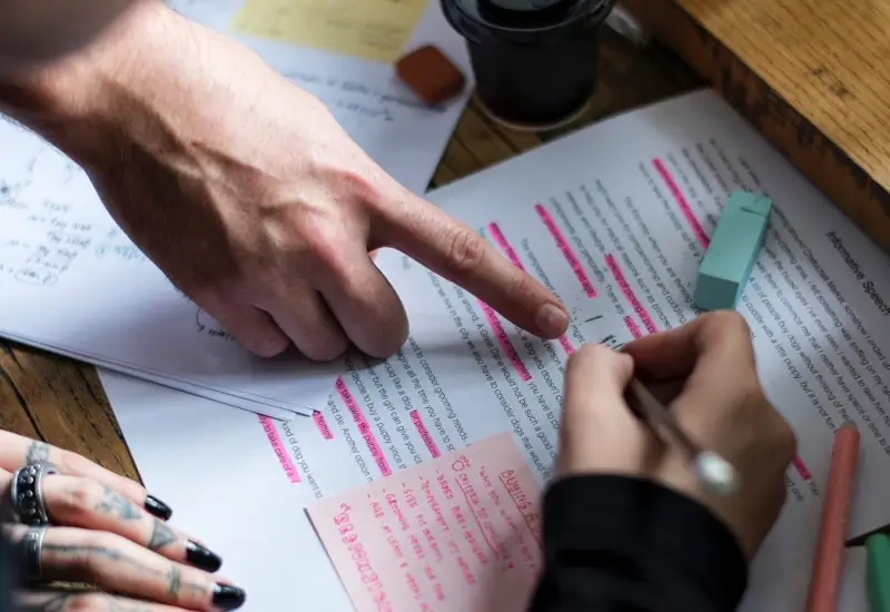 An image of a paper with many highlighted words with hands pointing at it